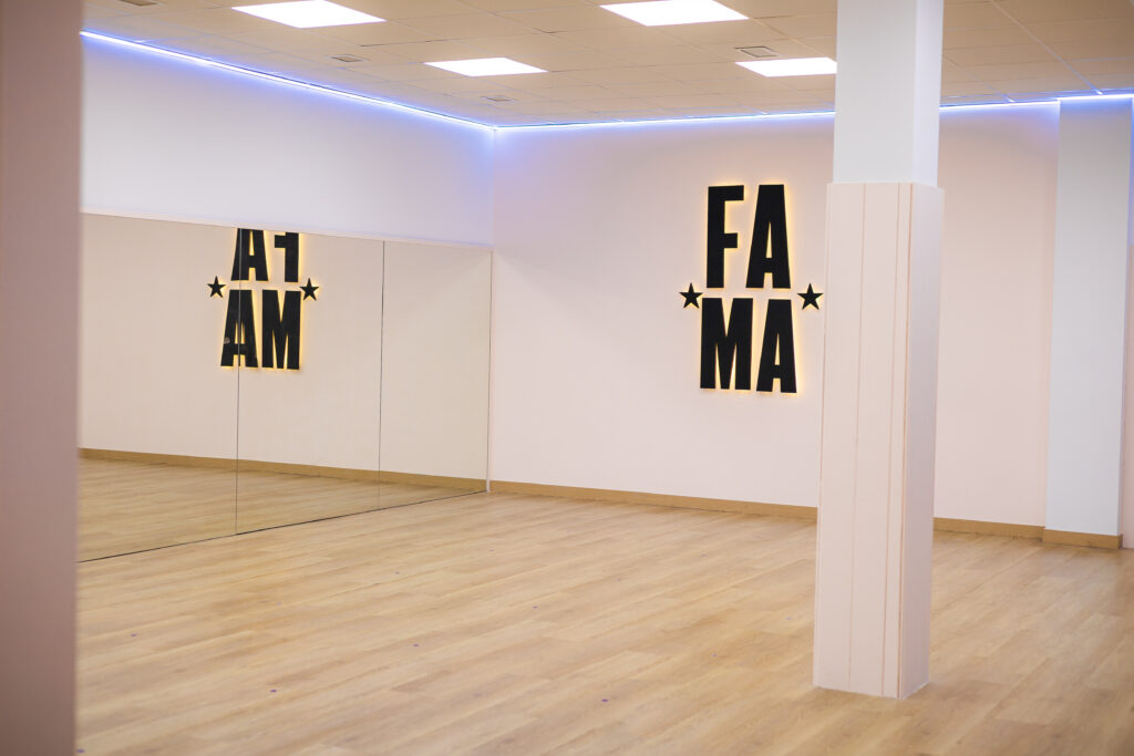 Sala de baile de FAMA en Molina de Segura, con espejos, suelo de madera y el logotipo iluminado de la academia